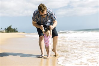 Father helping his baby girl walk on beach