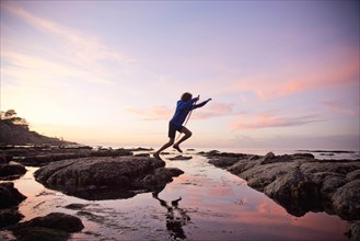 Teenage boy jumping between rocks of tide pool in La Jolla, California