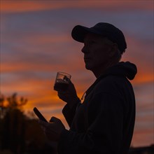 Silhouette of man holding coffee cup and smart phone at sunset
