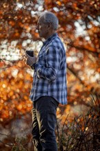 Man holding coffee cup by autumn trees