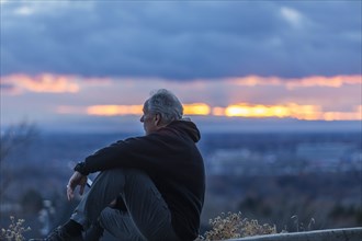 Seated man holding smart phone at sunset