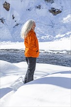 Mature woman wearing orange coat on snow by river