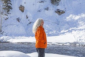 Mature woman wearing orange coat on snow by river