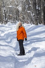 Mature woman wearing orange coat by bare trees in snow