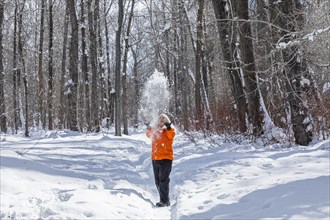 Mature woman wearing orange coat throwing snow by bare trees