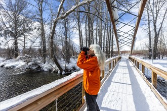 Mature woman using binoculars on snow covered footbridge