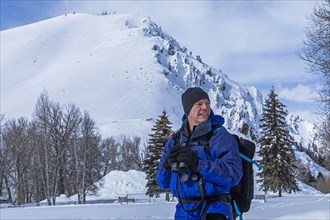 Senior man holding binoculars by snow covered mountain in Sun Valley, Idaho, USA