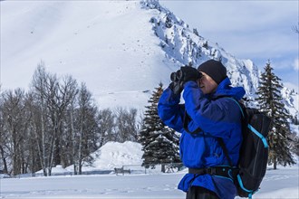 Senior man using binoculars by snow covered mountain in Sun Valley, Idaho, USA