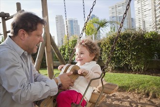 Father by daughter on swing in city park