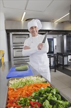 Smiling chef holding kitchen knife by raw vegetables