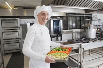Smiling chef holding tray of vegetables