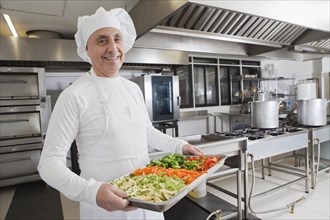 Smiling chef holding tray of vegetables