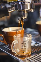 Coffee pouring from portafilter into coffee cup and beaker