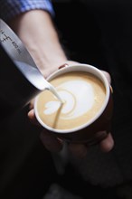 Barista pouring milk into coffee
