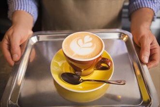 Barista holding yellow cup of coffee on tray