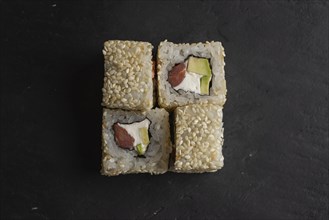 Sushi with sesame seeds on black surface