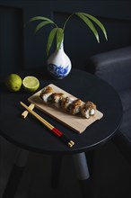 Sushi on table with chopsticks, vase and lime