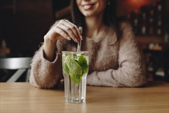 Woman holding straw in cocktail with mint leaves