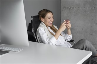 Laughing businesswoman using smartphone at desk