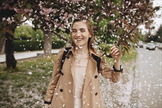Smiling woman among falling petals from tree in bloom