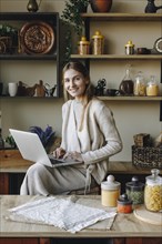 Smiling young woman using laptop in kitchen