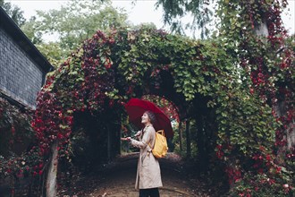 Woman holding umbrella by vine covered arch