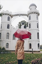 Woman holding red umbrella by Schloss Pfaueninsel in Potsdam, Germany