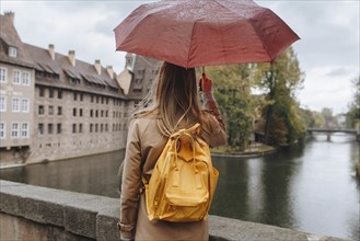 Woman wearing backpack holding umbrella by river in Nuremberg, Germany