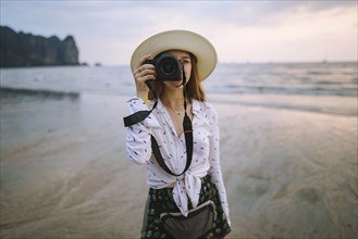Young woman photographing on beach in Krabi, Thailand