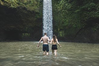 Young couple holding hands in river by Tibumana Waterfall in Bali, Indonesia