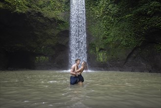 Young couple embracing in river by Tibumana Waterfall in Bali, Indonesia