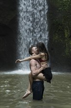 Young couple kissing in river by Tibumana Waterfall in Bali, Indonesia