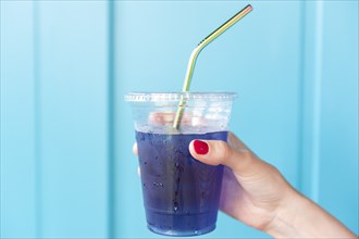 Woman holding blue drink in plastic cup with metal straw