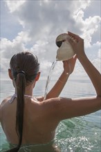 Woman in sea pouring water out of nautilus seashell