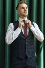 Man wearing pinstripe waistcoat adjusting his tie
