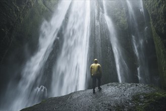 Man wearing yellow raincoat by Seljalandsfoss waterfall in Iceland