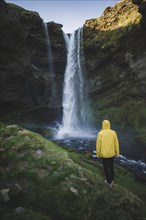 Man wearing yellow raincoat by Kvernufoss waterfall in Iceland