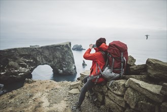 Female hiker photographing natural arch in Vik, Iceland