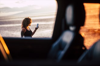 Woman using smart phone behind car window at sunset