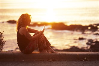 Woman using smart phone by beach at sunset