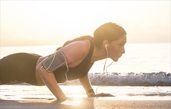Woman wearing headphones doing push-up on beach