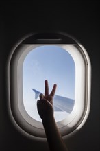 Silhouette of girl's hand doing peace sign by airplane window