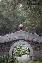 Woman wearing conical hat on arch bridge in Summer Palace gardens, Beijing, China