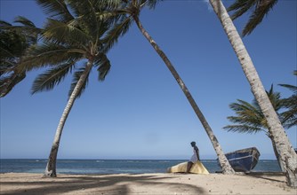 Woman sitting on boat under palm trees on beach in Las Terrenas, Dominican Republic