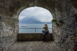 Woman sitting under arch by Lake Como, Italy