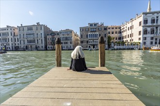 Woman sitting on jetty on Grand Canal in Venice, Italy