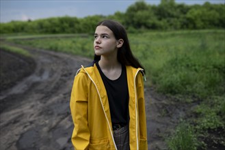 Teenage girl wearing yellow raincoat on country road