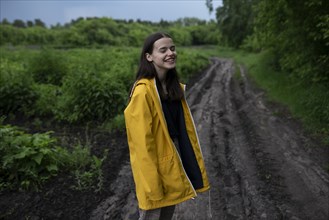Smiling teenage girl wearing yellow raincoat on country road