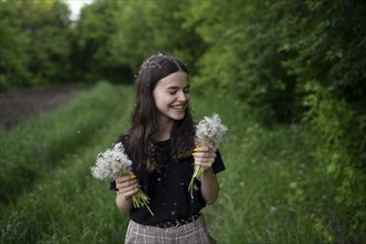 Smiling teenage girl holding dandelions in a field