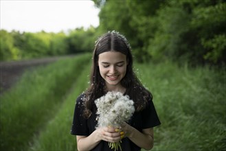 Smiling teenage girl holding dandelions in a field